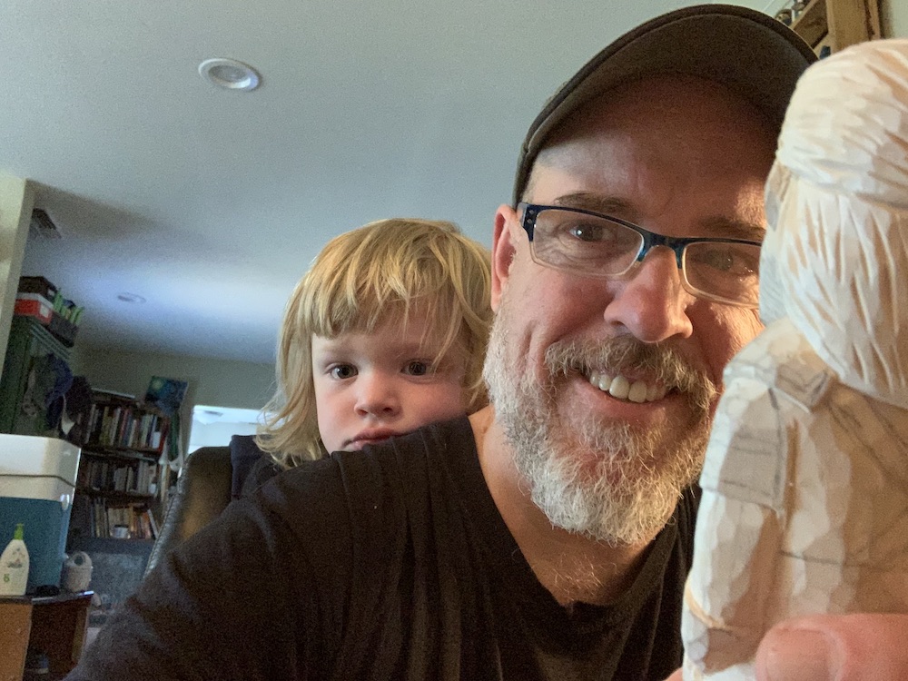 Marc with his young son Max, holding an unfinished woodcarving